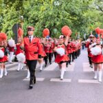 zdjęcie przedstawiające maszerujące dziewczęta z pomponami oraz idącą z nimi orkiestrę dętą