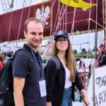 zdjęcie dwójki młodych ludzi spacerująceych nieopodal zacumowanych statków