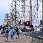 zdjęcie przedstawiające zacumowane statki do wybrzeża, oraz spacerujących ludzi