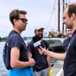 zdjęcie przedstawiające dwójkę mężczyzn udzielających wywiadu młodemu dziennikarzowi na nabrzeżu