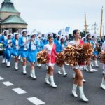 zdjęcie przedstawiające maszerujące dziewczęta z pomponami oraz idącą z nimi orkiestrę dętą