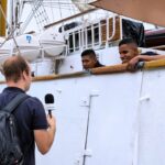 zdjęcie przedstawiające dwóch mężczyzn z załogi statku udzielających wywiadu młodemu dziennikarzowi