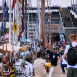 zdjęcie przedstawiające zacumowane łódki oraz spacerujących ludzi po nabrzeżu