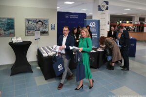 Konferencja podczas 40-lecia Instytutu Nauk o Polityce i Bezpieczeństwie Uniwersytetu Szczecińskiego. Korytarz. Czworo uczestników odbiera zestawy konferencyjne, m.in. książki jubileuszowe i torby z logiem 40-lecia Instytutu.