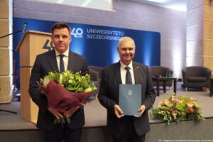 Uroczystość 40-lecia Instytutu Nauk o Polityce i Bezpieczeństwie Uniwersytetu Szczecińskiego. Na zdjęciu po lewej rektor uczelni z teczką i dyrektor instytut z kwiatami. W tle scena i granatowa ścianka z napisem: 40 lat Uniwersytetu Szczecińskiego.