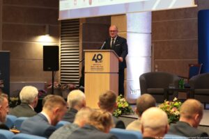 Uroczystość 40-lecia Instytutu Nauk o Polityce i Bezpieczeństwie Uniwersytetu Szczecińskiego. Aula (ujęcie bokiem). Na pierwszym planie uczestnicy tłem do kadru. W tle za mównicą prezydent Szczecina.
