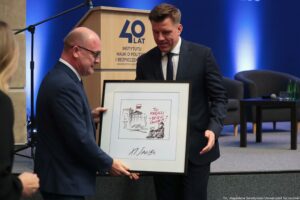 Uroczystość 40-lecia Instytutu Nauk o Polityce i Bezpieczeństwie Uniwersytetu Szczecińskiego. Aula. Prezydent Szczecina (po lewej) wręcza dyrektorowi Instytutu grafikę. W tle scena i mównica z napisem: 40 lat Uniwersytetu Szczecińskiego.
