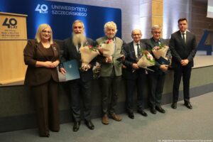 Konferencja podczas 40-lecia Instytutu Nauk o Polityce i Bezpieczeństwie Uniwersytetu Szczecińskiego. Aula. Przed sceną prorektorka (po lewej), dyrektor Instytutu (po prawej) i czterech prelegentów z kwiatami (w środku). W tle granatowa ścianka z napisem: 40 lat Uniwersytetu Szczecińskiego.