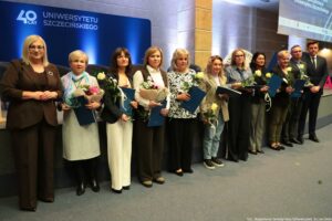 Uroczystość 40-lecia Instytutu Nauk o Polityce i Bezpieczeństwie Uniwersytetu Szczecińskiego. Aula. Przed sceną prorektorka (po lewej), dyrektor Instytutu (po prawej) i 9 pracowników z kwiatami i teczkami (w środku). W tle granatowa ścianka z napisem: 40 lat Uniwersytetu Szczecińskiego.