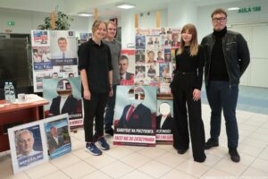 40-lecie Instytutu Nauk o Polityce i Bezpieczeństwie Uniwersytetu Szczecińskiego. Na zdjęciu czworo przedstawicieli jednego z kół naukowych (2 studencki, 2 studentów), którzy stoją na tle plansz z plakatami i ulotkami wyborczymi absolwentów uczelni.