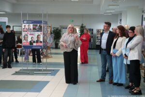 40-lecie Instytutu Nauk o Polityce i Bezpieczeństwie Uniwersytetu Szczecińskiego. Korytarz. W środku prorektorka ds. kształcenia Uniwersytetu Szczecińskiego wita zebranych. Po lewej wystawa plansz z plakatami i ulotkami wyborczymi absolwentów uczelni.