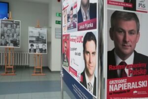 40-lecie Instytutu Nauk o Polityce i Bezpieczeństwie Uniwersytetu Szczecińskiego. Korytarz. Po prawej fragment wystawy plansz z plakatami i ulotkami wyborczymi absolwentów uczelni. W tle wystawa nawiązująca do historii Instytutu.
