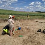 3 osoby wykonujące prace archeologiczne w otwartej przestrzeni.