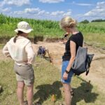 Dwie kobiety przyglądające się wykopaliskom w terenie.