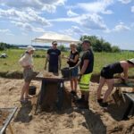 Grupa ludzi przyglądająca się zebranym podczas wykopalisk znaleziskom.