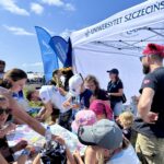 zdjęcie stoiska US, na pierwszym planie grupa ludzi robiąca bransoletki l