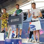 Stojący na scenie na podium trzej mężczyźni – uczestnicy 46. PKO Półmaratonu Szczecin, trzymający puchary i papierowe torby z upominkami.