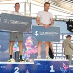 Stojący na scenie na podium dwaj mężczyźni – uczestnicy 46. PKO Półmaratonu Szczecin, trzymający granatowe plansze z logiem Klubu Absolwentów Uniwersytetu Szczecińskiego i Centrum Badań Strukturalno-Funkcjonalnych Człowieka Uniwersytetu Szczecińskiego.