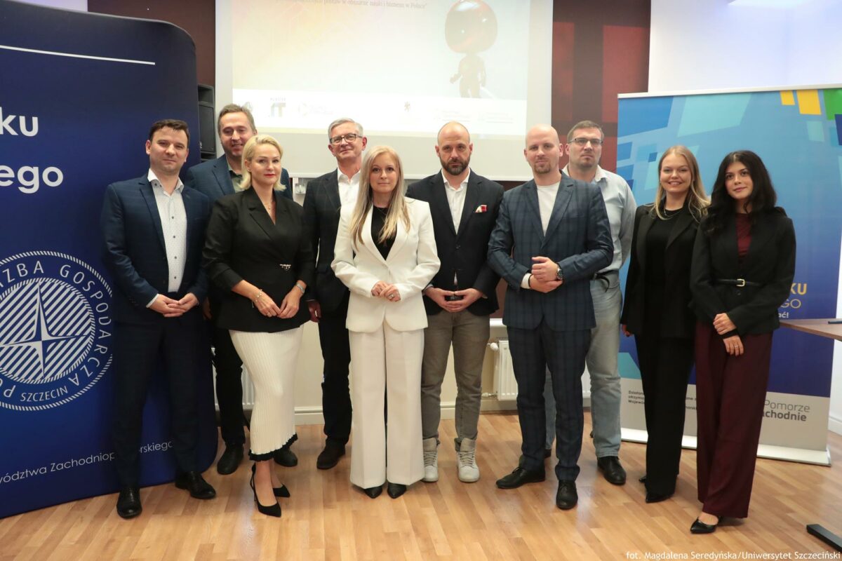 Grupa uczestników na konferencji o AI (4 kobiety, 6 mężczyzn). Za nimi na środku ekran, po prawej rollup Północnej Izby Gospodarczej, po lewej granatowa ścianka Północnej Izby Gospodarczej.