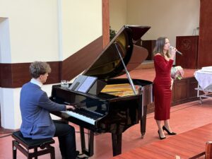 Sala Wydziału Ekonomii, Finansów i Zarządzania. Po lewej pianista za czarnym fortepianem (tyłem do kadru). Obok fortepianu (bokiem do kadru) wokalistka z mikrofonem.