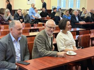 Sala Wydziału Ekonomii, Finansów i Zarządzania. Ujęcie ławki z krzesłami. Na pierwszym planie 3 osoby (dwóch mężczyzn i jedna kobieta). Na stole stoi talerzyk z kawałkiem tortu.