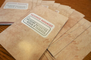 Leżące na drewnianym stole beżowe teczki stylizowane na postarzone. Na teczkach napis: Dziennik badaczy, Naukowy Detektyw – Misja w Terenie.