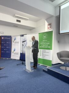 zdjęcie jednego z przemawiających prelegentów ( mężczyzna stojący przy mównicy z mikrofonem)