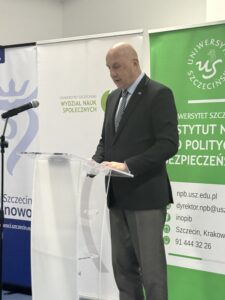 zdjęcie jednego z przemawiających prelegentów ( mężczyzna stojący przy mównicy z mikrofonem)