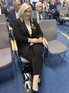 zdjęcie uczestników konferencji siedzących w sali wykładowej ( w centralnej części fotografii została ujęta kobieta siedząca na krześle)