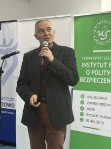 zdjęcie jednego z przemawiających prelegentów ( mężczyzna stojący przy mównicy z mikrofonem)