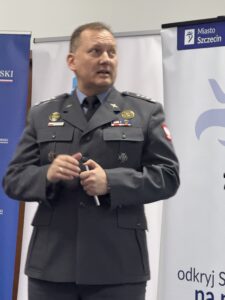 zdjęcie jednego z przemawiających prelegentów ( mężczyzna w mundurze stojący przy mównicy z mikrofonem)