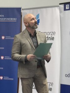 zdjęcie jednego z przemawiających prelegentów ( mężczyzna stojący przy mównicy z mikrofonem)