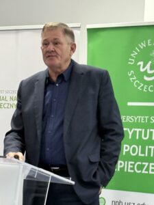 zdjęcie jednego z przemawiających prelegentów ( mężczyzna stojący przy mównicy z mikrofonem)