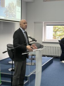 zdjęcie jednego z przemawiających prelegentów ( mężczyzna stojący przy mównicy z mikrofonem)