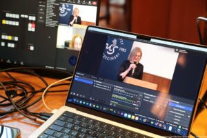 Laptop i ekran z obrazem rejestrowanym przez kamerę podczas III Międzynarodowego Kongresu Języka i Kultury Polskiej. Na obrazie dr Ewa Hendryk z mikrofonem.