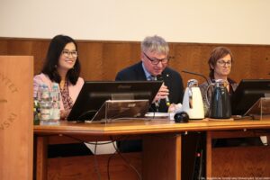 III Międzynarodowy Kongres Języka i Kultury Polskiej. Stół prezydialny. Po bokach dwie prelegentki, w środku prorektor ds. nauki US. Na stole ekrany i dzbanki z kawą i herbatą.