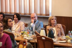 Ujęcie bokiem na sześć osób. Siedzący przy stole uczestnicy III Międzynarodowego Kongresu Języka i Kultury Polskiej. Na stole wody, soki oraz dzbanki z kawą i herbatą.