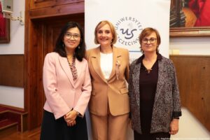 Dwie prelegentki III Międzynarodowego Kongresu Języka i Kultury Polskiej i gospodyni wydarzenia (w środku). Za nimi biały rollup z granatowym okrągłym logiem Uniwersytetu Szczecińskiego.