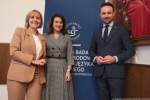 Troje uczestników III Międzynarodowego Kongresu Języka i Kultury Polskiej (ujęcie do kolan). Za nimi granatowy rollup z białym okrągłym logiem Uniwersytetu Szczecińskiego.