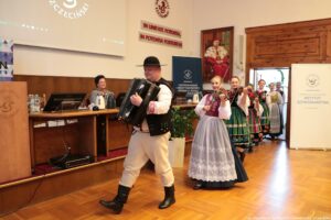 Wchodzący do sali, ubrany w stroje ludowe Zespół Pieśni i Tańca Szczecinianie. Z przodu mężczyzna z akordeonem, za nim kilka kobiet ze skrzypcami.