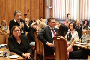 Ujęcie bokiem. Siedzący przy stołach (3 rzędy) uczestnicy III Międzynarodowego Kongresu Języka i Kultury Polskiej. Po lewej stojąca kobieta z mikrofonem zadająca pytanie podczas dyskusji.