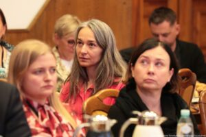 Siedzący przy stołach (ujęcie na 5 osób) uczestnicy III Międzynarodowego Kongresu Języka i Kultury Polskiej. Na pierwszym planie 3 kobiety słuchające wykładu.