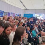 Kilkudziesięcioosobowa widownia podczas debaty na Forum Ekonomicznym. W tle – na ścianie – plakat promujący konkurs Matematyka w obiektywie i zdjęcia stanowiące wystawę.