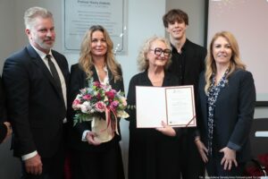 Uroczystość nadania auli im. Profesora Macieja Zielińskiego – Wydział Prawa i Administracji Uniwersytetu Szczecińskiego. Dziekan Wydziału dr hab. Ewelina Cała-Wacinkiewicz, prof. US (po prawej, przodem), 4-osobowa rodzina profesora (przodem po lewej) z kwiatami i elegancką teczką. W tle odsłonięta tablica.