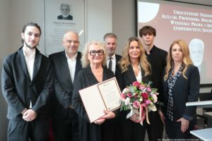 Uroczystość nadania auli im. Profesora Macieja Zielińskiego – Wydział Prawa i Administracji Uniwersytetu Szczecińskiego. Dziekan Wydziału dr hab. Ewelina Cała-Wacinkiewicz, prof. US (po prawej, przodem), 6-osobowa rodzina profesora (przodem po lewej) z kwiatami i elegancką teczką. W tle odsłonięta tablica.