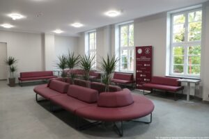 Otwarcie budynku Wydziału Prawa i Administracji Uniwersytetu Szczecińskiego. Na środku bordowe kanapy ustawione owalnie. W środku cztery wysokie kwiaty doniczkowe. Pod oknami pojedyncze bordowe kanapy.