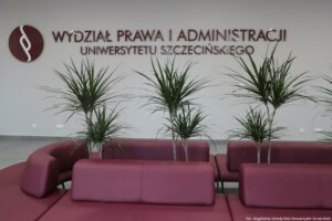 Otwarcie budynku Wydziału Prawa i Administracji Uniwersytetu Szczecińskiego. Na zdjęciu bordowe kanapy ustawione owalnie. W środku cztery wysokie kwiaty doniczkowe. W tle na ścianie bordowy napis Wydział Prawa i Administracji Uniwersytetu Szczecińskiego.
