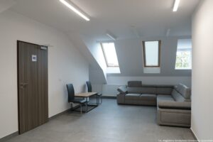 Otwarcie budynku Wydziału Prawa i Administracji Uniwersytetu Szczecińskiego. Korytarz. Po lewej wejście do WC, dwa czarne krzesła i pośrodku nich kwadratowy drewniany stolik. Po prawej szary narożnik. Na wprost okna.