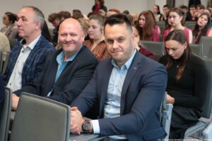 Otwarcie budynku Wydziału Prawa i Administracji Uniwersytetu Szczecińskiego. Ujęcie bokiem. Uczestnicy siedzący w rzędach w sali.