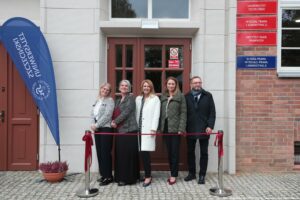 Otwarcie budynku Wydziału Prawa i Administracji Uniwersytetu Szczecińskiego. Wejście do budynku, przed którym jest czerwona wstęga. Za wstęgą dziekan Wydziału dr hab. Ewelina Cała-Wacinkiewicz, prof. US i prodziekani. Po lewej granatowa flaga z białym logiem uczelni.